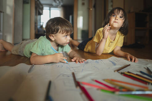 Brothers drawing with colored pencils lying on floor at home - ANAF01799