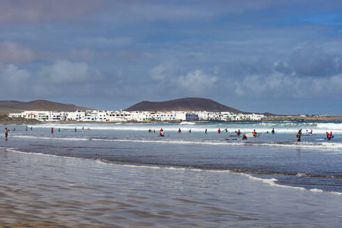 Spain, Canary Islands, Caleta de Famara, People swimming and surfing at Playa de Famara beach - WGF01469