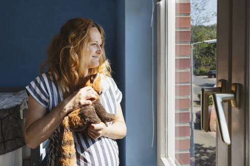 Pregnant woman holding stuffed toy at home - IHF01485