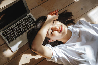 Freelancer napping by laptop lying on hardwood floor at home - NLAF00082