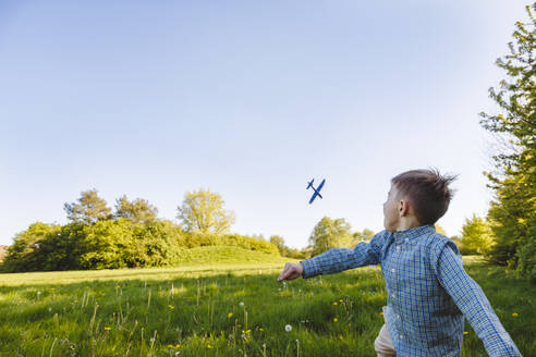 Junge spielt mit Spielzeugflugzeug im Garten - IHF01499