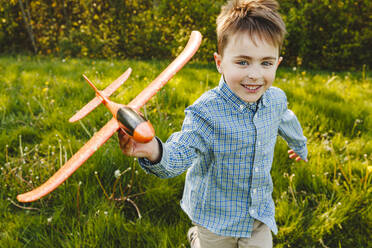 Lächelnder Junge spielt mit Spielzeugflugzeug im Garten - IHF01500