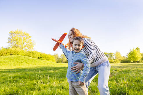 Lächelnde Mutter und Sohn spielen mit Spielzeugflugzeug im Garten - IHF01501