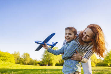 Smiling mother holding son playing with toy airplane - IHF01502