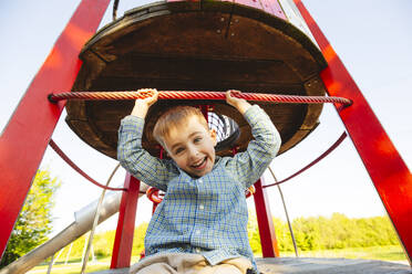 Glücklicher Junge sitzt und hat Spaß auf dem Spielplatz - IHF01506