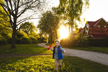 Glücklicher Junge läuft mit Spielzeugflugzeug bei Sonnenuntergang - IHF01510