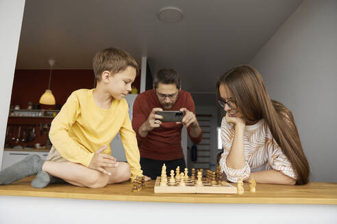 Mutter und Sohn spielen Schach, der Vater fotografiert mit dem Smartphone - SANF00152