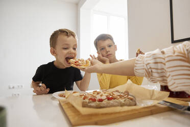 Hand einer Frau, die ihren Sohn zu Hause mit Pizza füttert - SANF00159