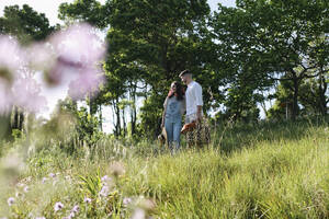 Boyfriend and girlfriend standing on grass at sunny day - ASGF03887