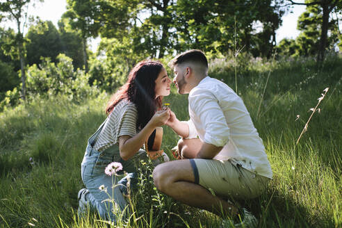Zärtliches Paar küsst sich kauernd auf Gras im Park - ASGF03897