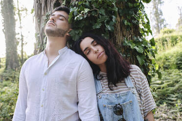 Woman leaning on boyfriend's shoulder near tree in forest - ASGF03910