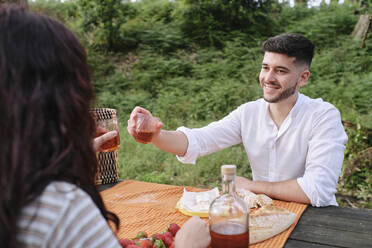 Lächelnder junger Mann, der mit seiner Freundin im Wald auf ein Getränk anstößt - ASGF03923