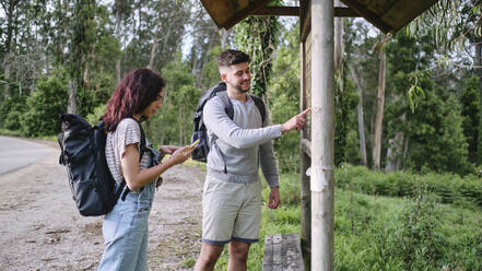 Mann zeigt auf Karte mit Freundin, die ein Smartphone benutzt - ASGF03930