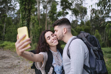 Ein Mann hält einen süßen Moment mit seiner Freundin fest, während er ein Selfie mit ihrem Smartphone macht - ASGF03932