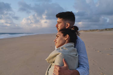 Man embracing girlfriend at beach - ASGF03944