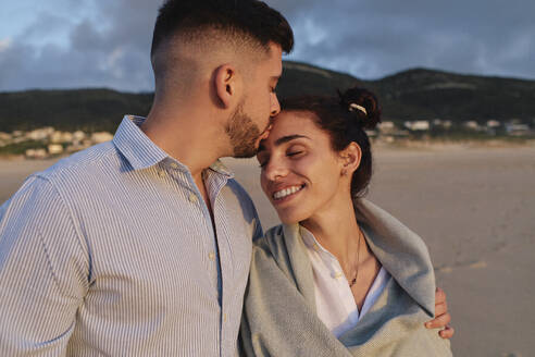 Man kissing on girlfriend's forehead at beach - ASGF03947