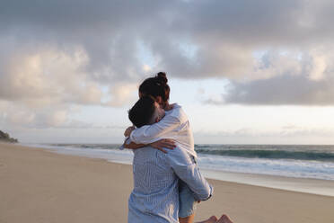 Young man picking up girlfriend in arms at beach - ASGF03949
