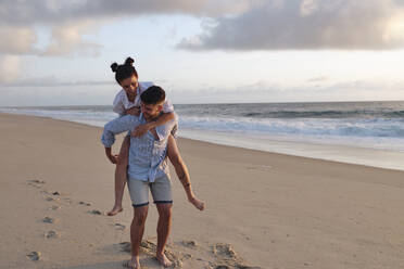 Man giving piggyback ride to girlfriend at beach - ASGF03954