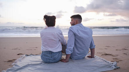 Boyfriend and girlfriend sitting on blanket at beach - ASGF04001