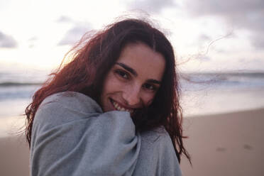 Happy woman wrapped in blanket at beach - ASGF04027