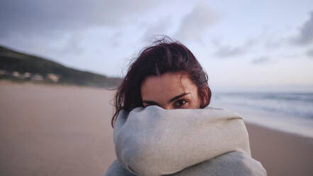 Junge Frau bedeckt ihr Gesicht mit einer Decke am Strand - ASGF04030