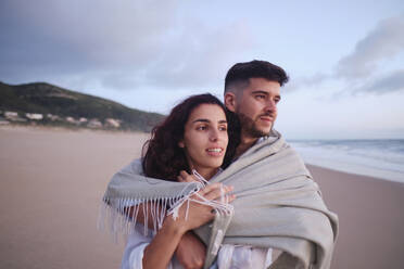 Young couple covered in blanket at beach - ASGF04038