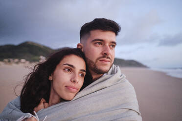 Contemplative couple covered in blanket at beach - ASGF04039