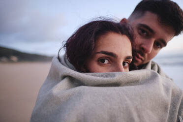 Man and woman wrapped in blanket at beach - ASGF04045