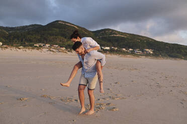 Man giving piggyback ride to woman at beach - ASGF04046