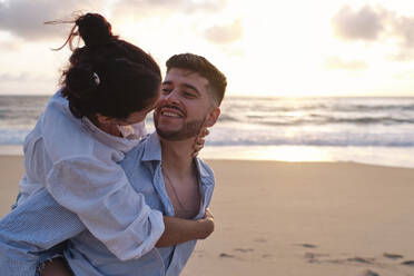 Smiling man giving piggyback ride to woman at beach - ASGF04048