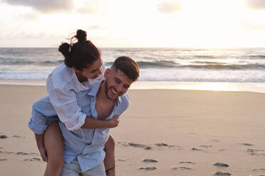 Happy young man giving piggyback ride to woman at beach - ASGF04050