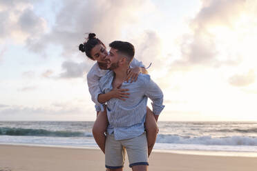 Lächelnder Mann, der seine Freundin am Strand huckepack nimmt - ASGF04052