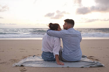 Man with arm around woman sitting at beach - ASGF04069