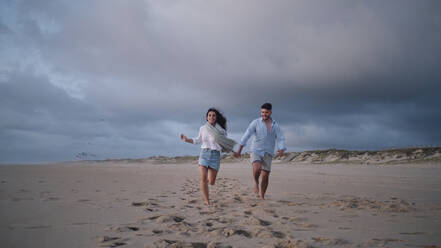 Glückliches junges Paar läuft zusammen am Strand - ASGF04079