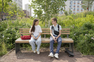 Smiling friends sitting on bench at park - LESF00357