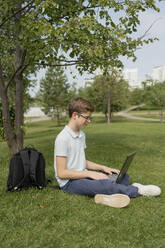 Junge mit Laptop im Gras sitzend im Park - LESF00360