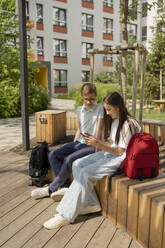 Mädchen, das ein Smartphone benutzt, sitzt mit einem Freund auf einer Bank im Park - LESF00368