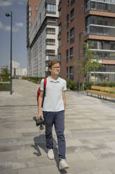 Boy walking on footpath holding skateboard - LESF00369