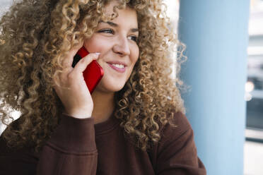 Lächelnde junge Frau mit lockigem Haar, die am Telefon spricht - AMWF01633
