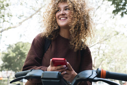 Thoughtful young woman holding smart phone at bike - AMWF01654