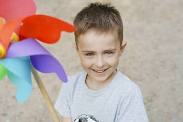 Lächelnder Junge mit buntem Regenbogen-Pinwheel-Spielzeug - IHF01513