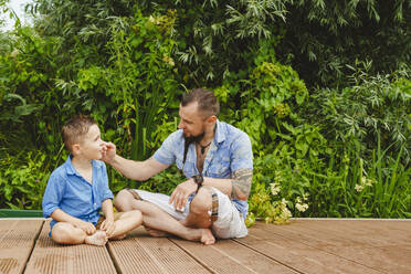 Father and son sitting on footbridge in front of plants - IHF01541