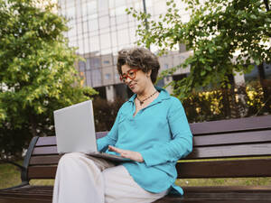Lächelnde Geschäftsfrau mit Laptop auf einer Parkbank sitzend - IEF00466