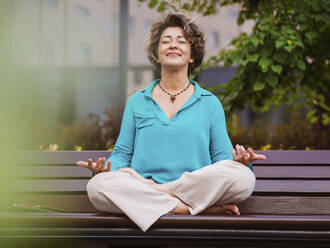 Reife Geschäftsfrau meditiert auf einer Parkbank - IEF00474