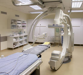 Ein modernes Krankenhauszimmer, ein großes tragbares mobiles Scangerät mit gebogenen Armen, ein mobiler Scanner und eine Krankenhausliege oder ein Bett. - MINF16624