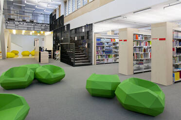A healthcare college library with open spaces, green chairs and book stacks. A modern light and airy building. - MINF16632