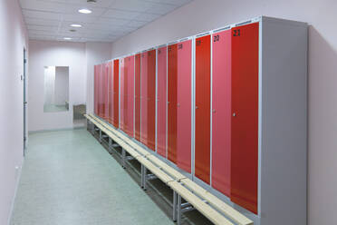 Sports and exercise facilities indoors. Gym. Changing room, locker room. Red cupboard doors. Bench seat. - MINF16634