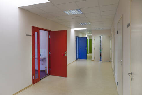 A school corridor with coloured doors opening off it. Red, blue and green doors. Lockers and cupboards. - MINF16641