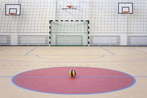 Eine Schulsporthalle mit einem markierten Hallenfußballplatz, Tor und Basketballkörben, einem blau-gelb gestreiften Ball in einem rosa Kreis. - MINF16642