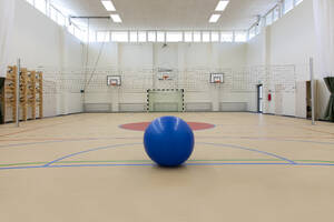 Sports facilities in a high school, a large gym with sports courts, basketball hoops and a goal, a blue ball. - MINF16643